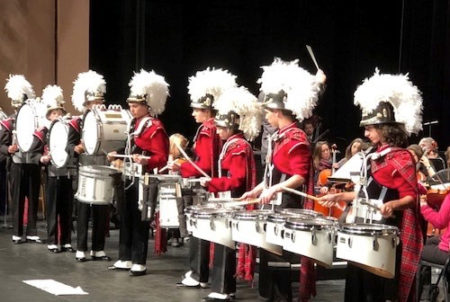 students in band uniforms line stage with drums