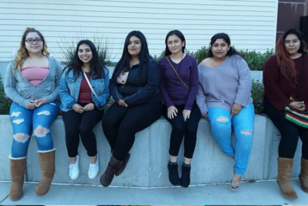 six students sitting along concrete wall