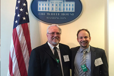 two administrators in front of American flag and white house seal